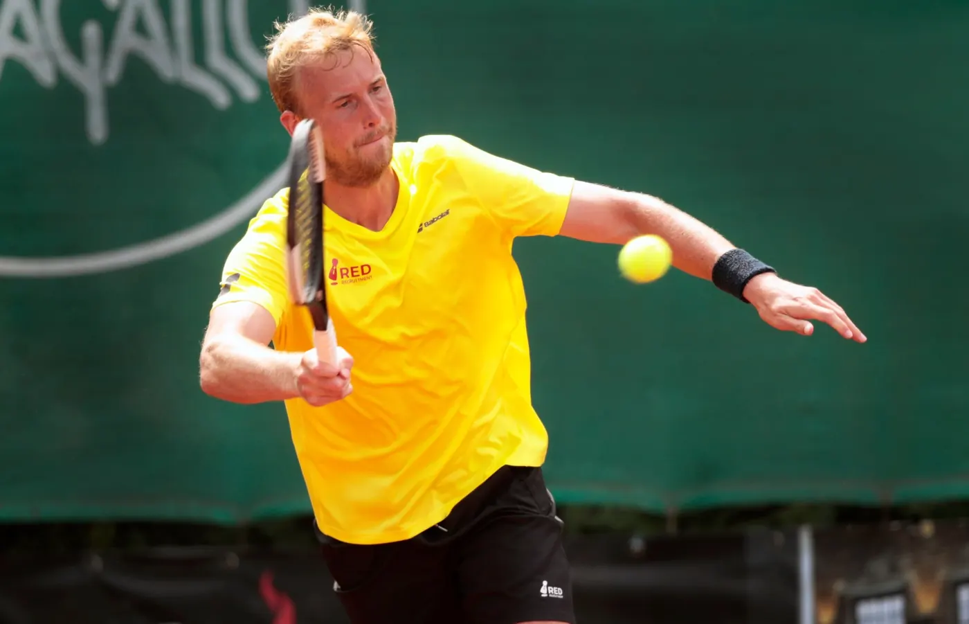 Tennisspeler in een geel shirt slaat een forehand op de baan